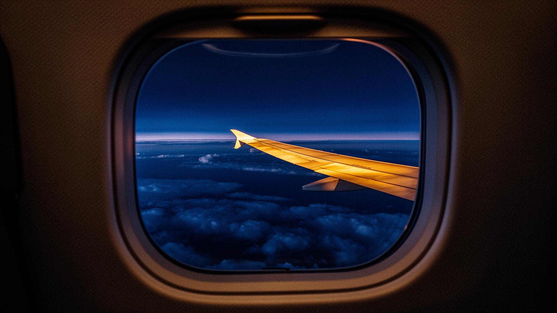 View from a private cabin window onto a gold-lit wing above twilight clouds